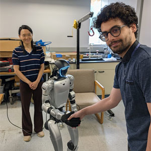 Two people pose with a small humanoid robot in a robotics laboratory.