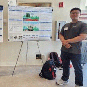 Person standing beside a research poster on an easel, with a backpack on the floor beneath it.