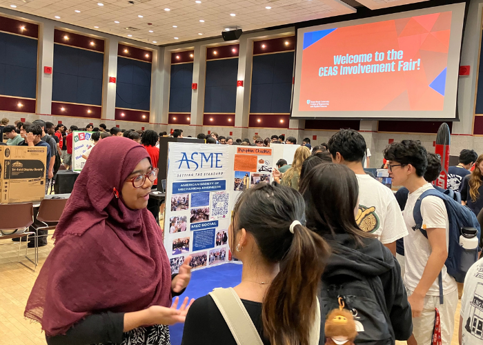 Students gather at an engineering involvement fair in an auditorium, with an ASME display and a screen welcoming attendees.