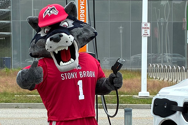wolfie mascot holding EV charger and giving thumbs up