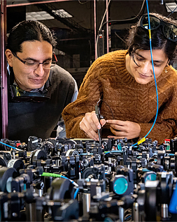 two students working on a table full of electronic metal widgets
