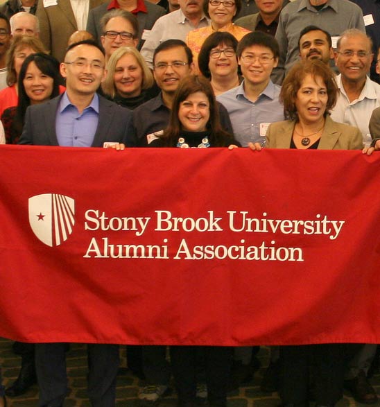 Group of smiling alumni holding up a Stony Brook Alumni Association banner