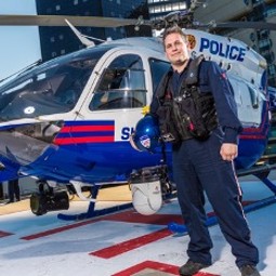 Man with cropped brown hair wearing EMT uniform standing in front of red, white and blue police helicopter