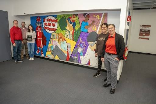 art tank winner and cbc members standing next to the mural of sbu students and mascot as superheros