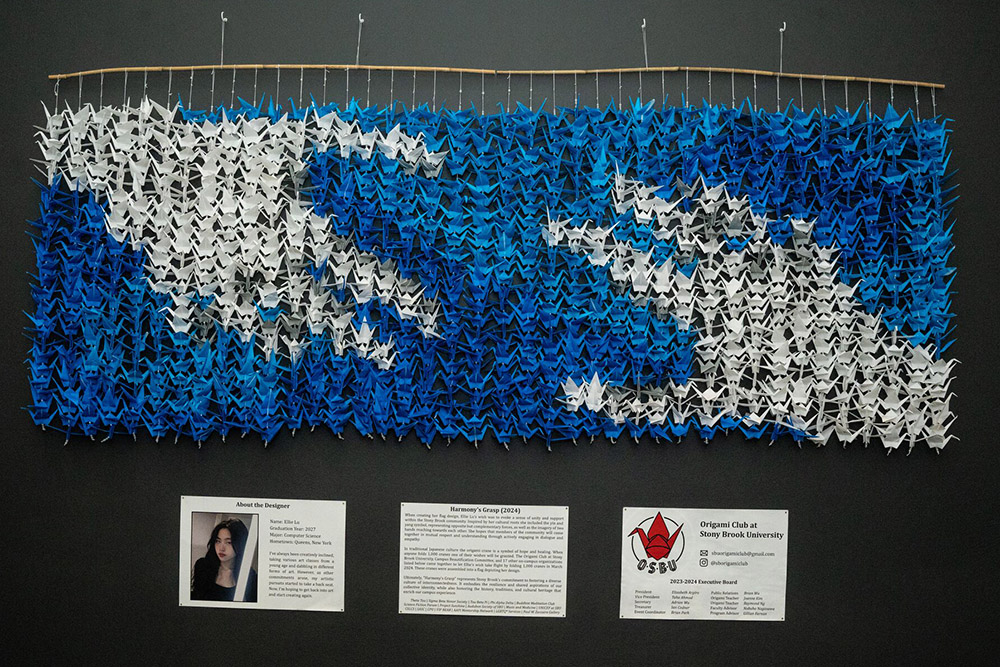 origami art hanging from a bar, with two hands reaching at each other potrayed in it