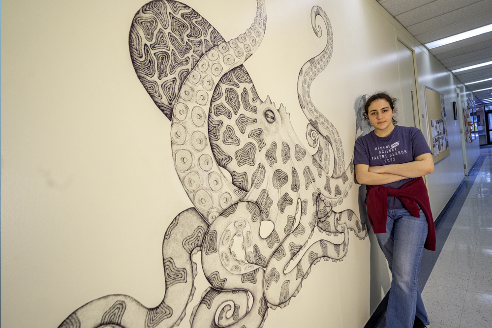 student standing next to the black and white actupus mural