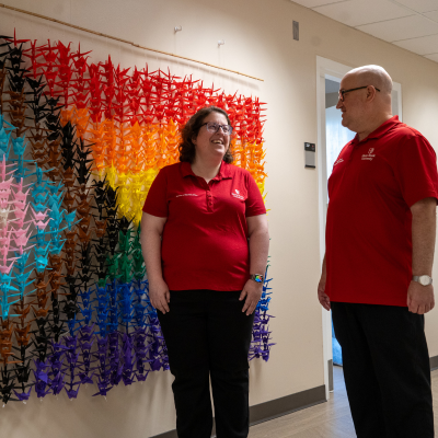 Two caps staff standing in front of an origami flag in the hallway