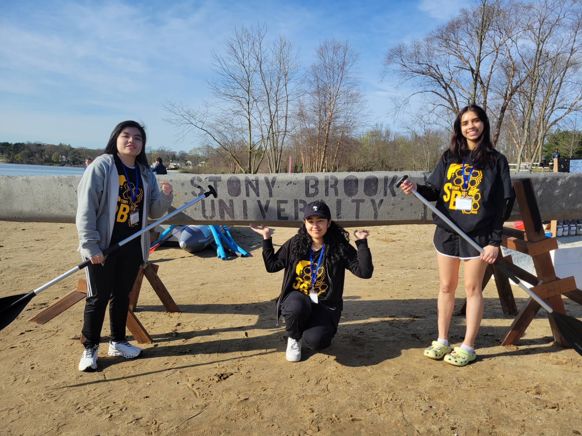 Three students standing in front of a concrete conue with Stony Brook University painted on the front.