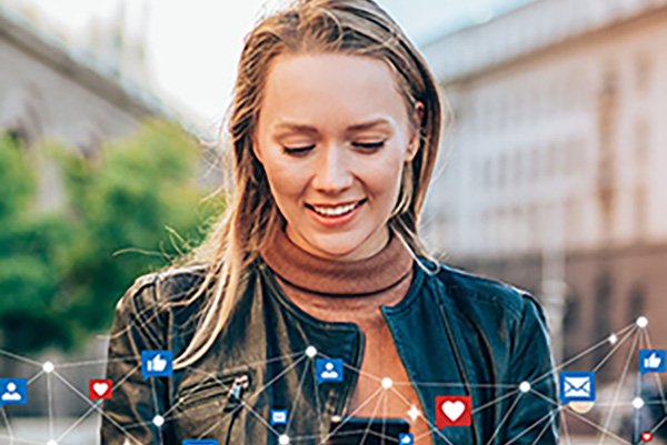 Technology and Society A woman smiling (head and shoulders) looking at her cell phone and images of social media icons such as hearts and thumbs up form a border at bottom