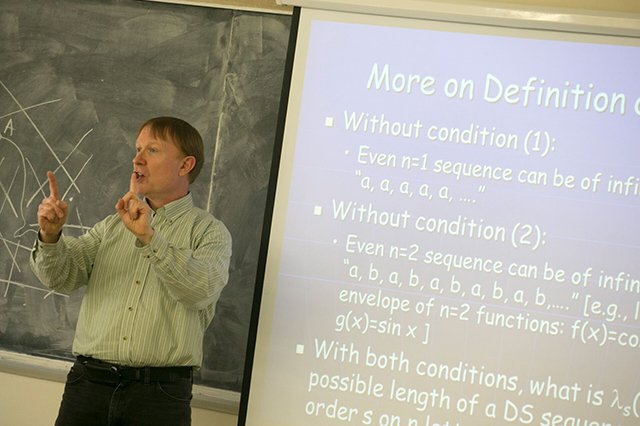 Applied Math and Statistics Faculty Joseph Mitchell, Chair of AMS, teaching in front of a blackboard with a slide to his right with mathematics