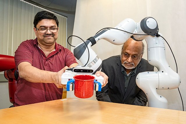 Computer Science Faculty Two professors with a robotic arm are seated at a table