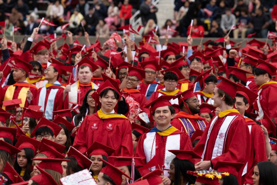 Commencement A large group of graduates in red caps and gowns celebrate, many smiling and holding small flags.