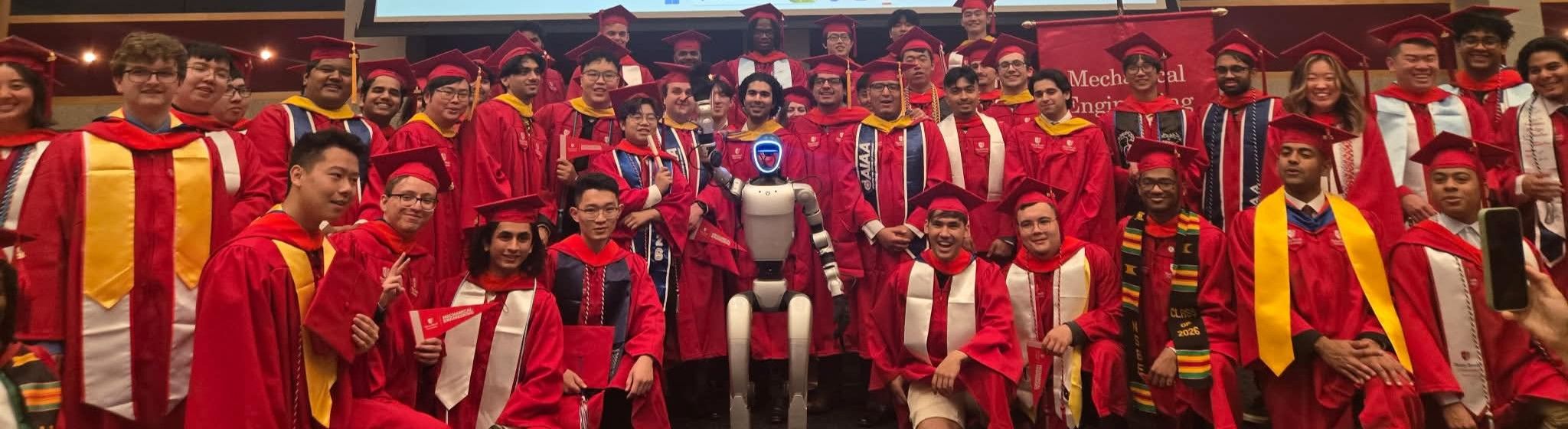 A group of graduates in red gowns and caps, with a humanoid robot in the center.