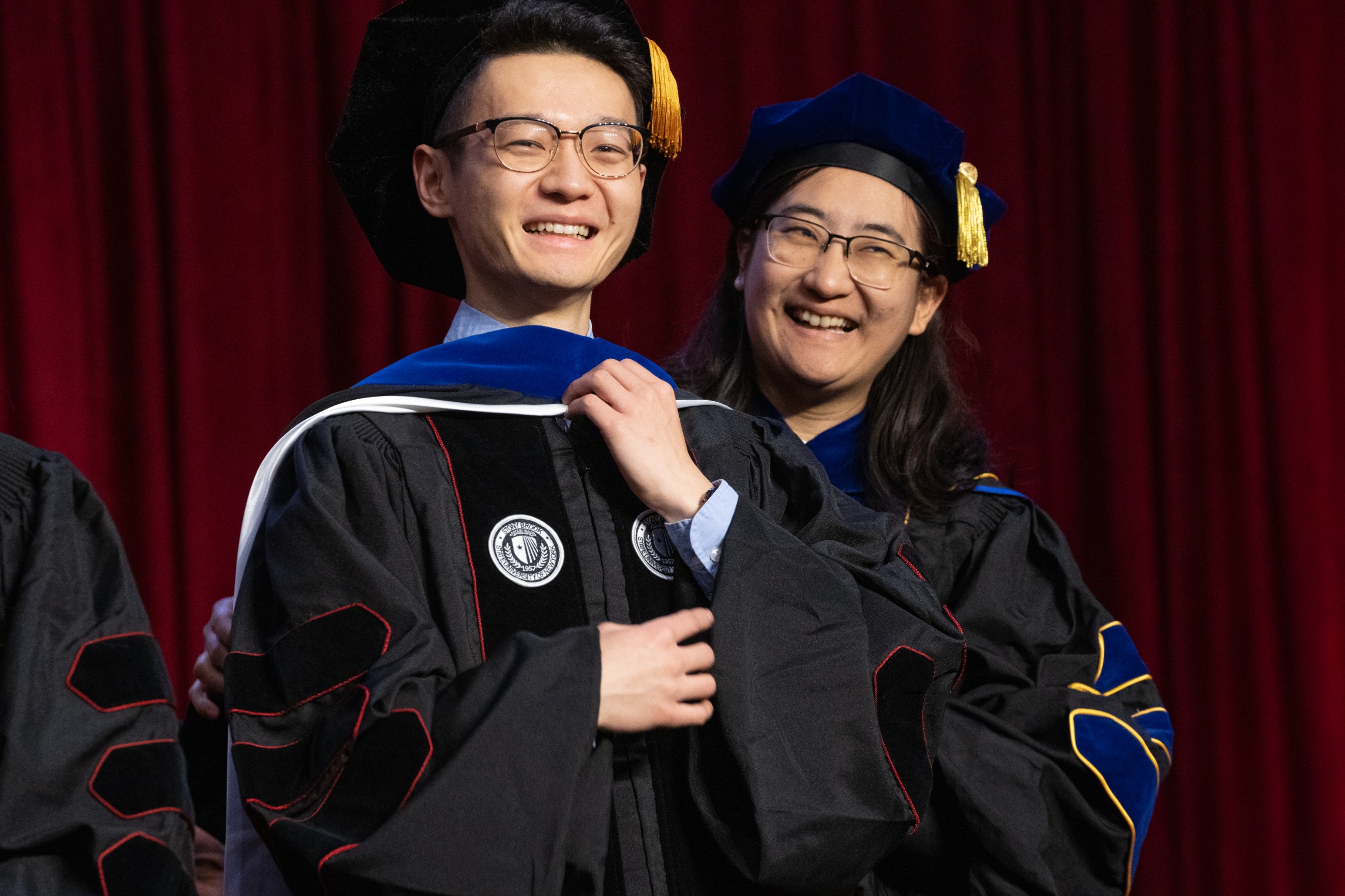 PhD candidate and advisor smiling on stage at hooding ceremony