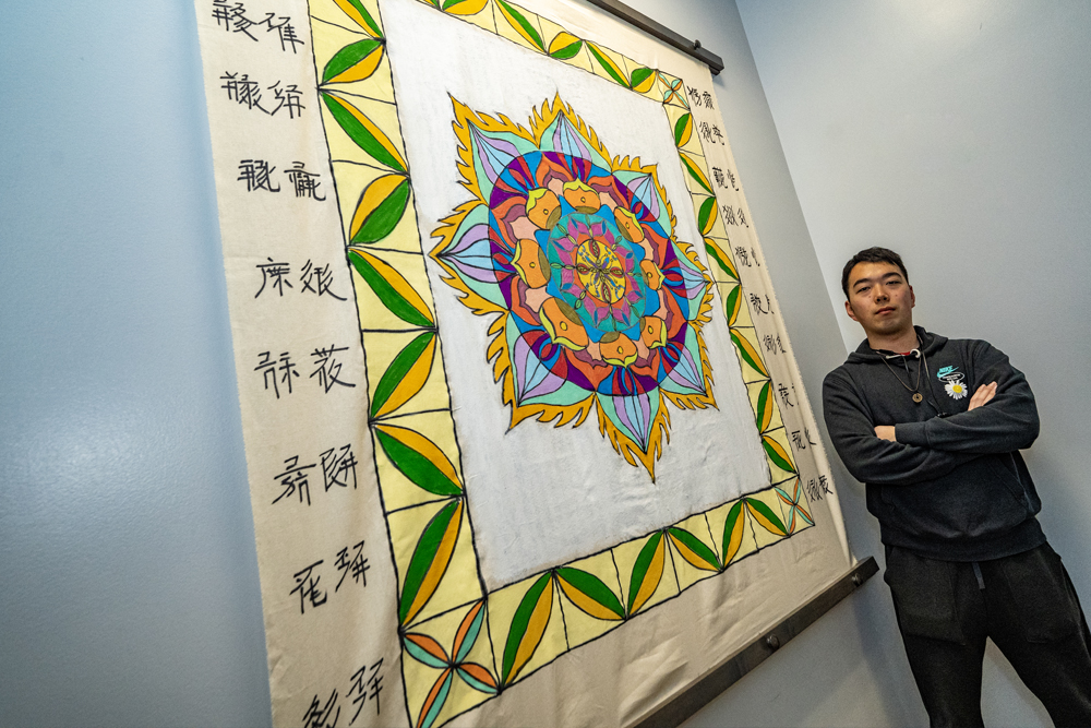 image of man standing in front of a canvas hung on a wall depicting a mandala image