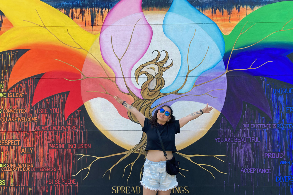 image of a woman standing in front of a mural on a wall depicting a bird spreading its wings