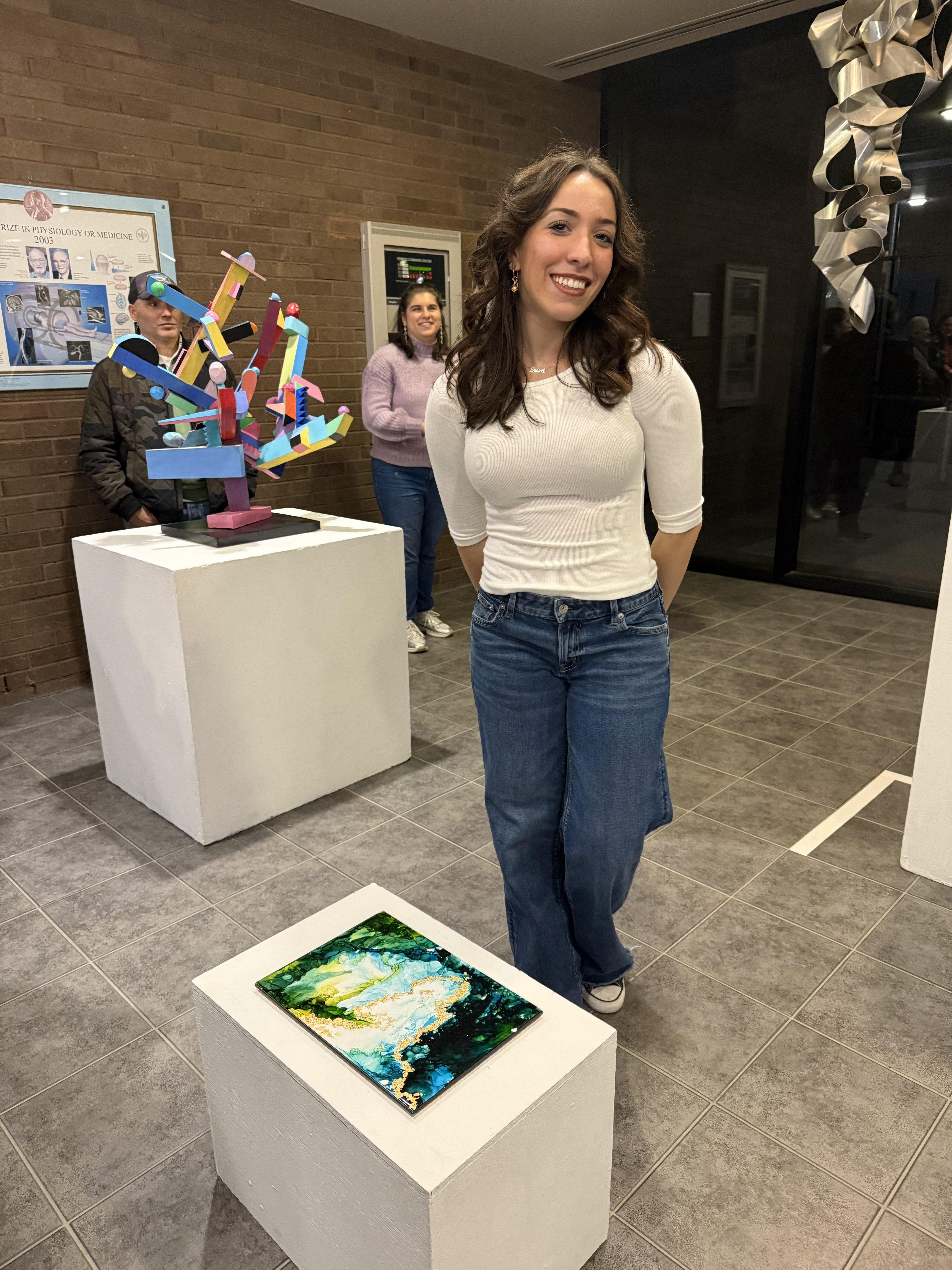 Eleni Tsevis Art Art student, Eleni Tsevis wearing a white shirt and jeans stands next to her green and gold acrylic art sculpture