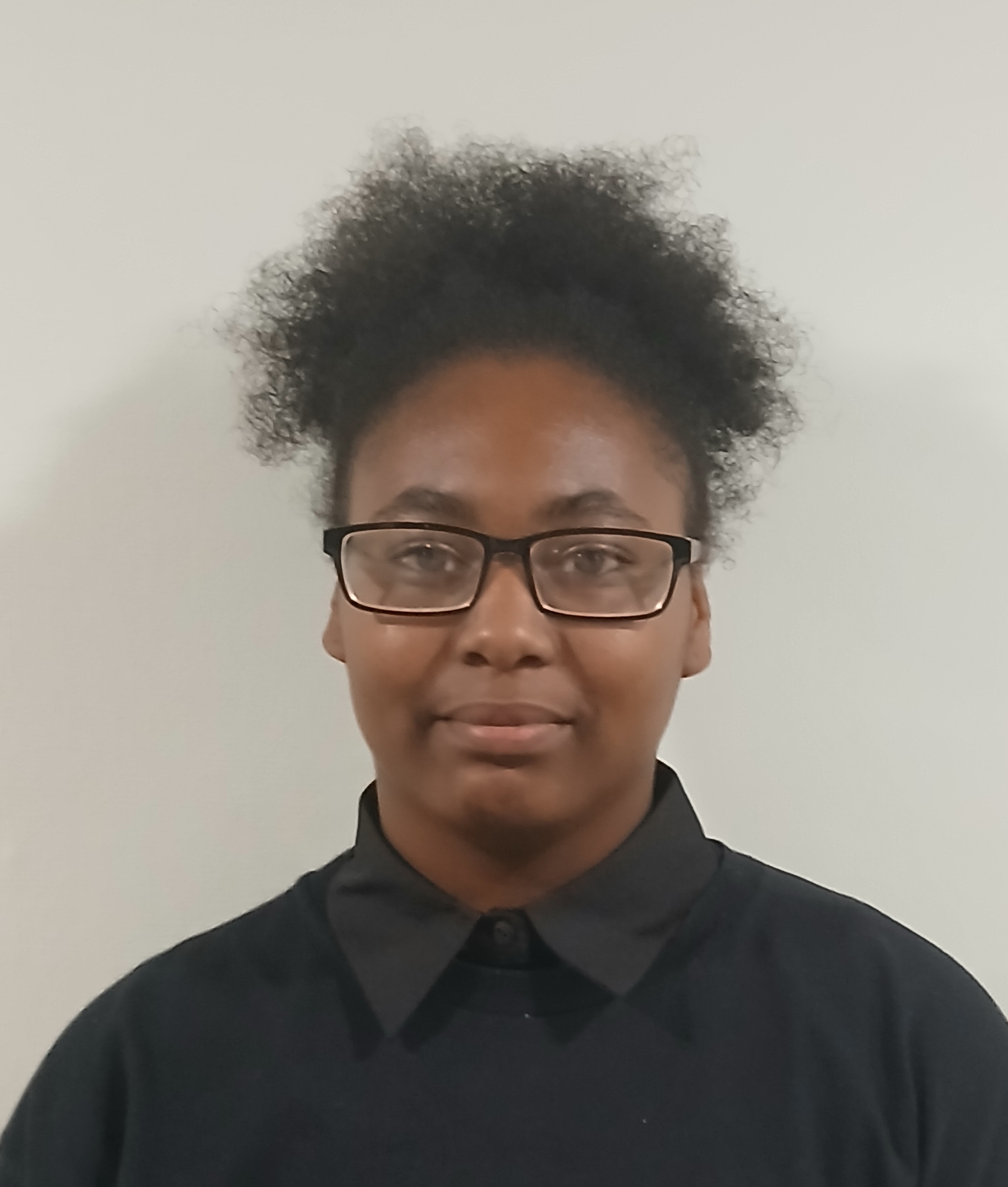 a woman wearing black eyeglasses stands in front of a white wall