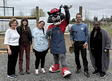 Wolf mascot poses for photo in community garden.