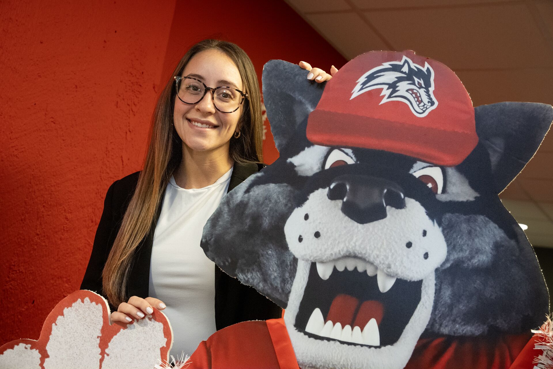 A woman with glasses smiling while posing next to a cutout of Wolfie, the Stony Brook University mascot.