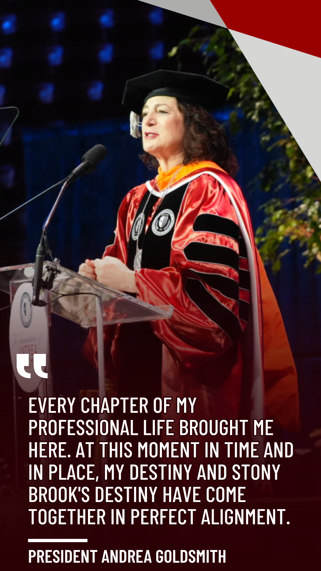 President Andrea Goldsmith stands at a transparent podium speaking into a microphone while wearing academic regalia.