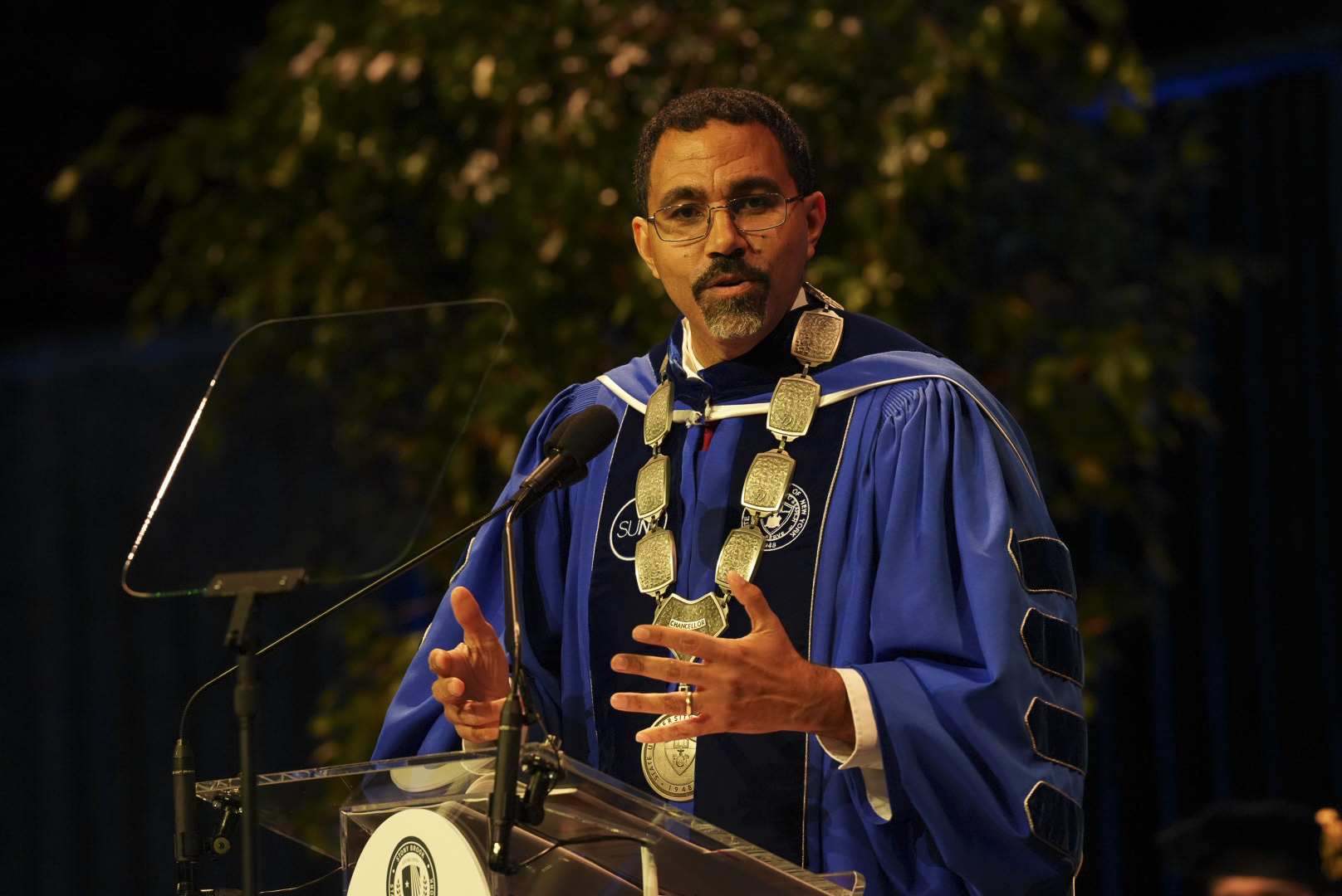 SUNY Chancellor John B. King Jr. speaks from a podium during an official academic ceremony.