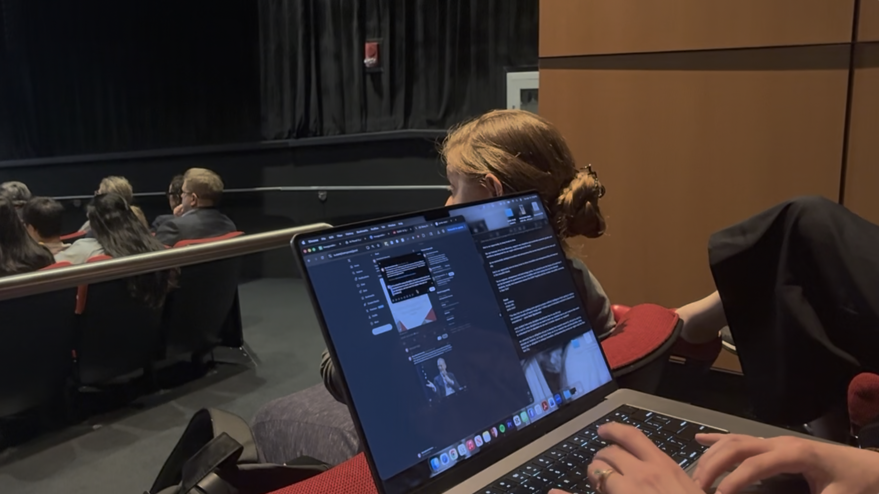 An attendee uses a laptop inside a dimly lit auditorium during an event.
