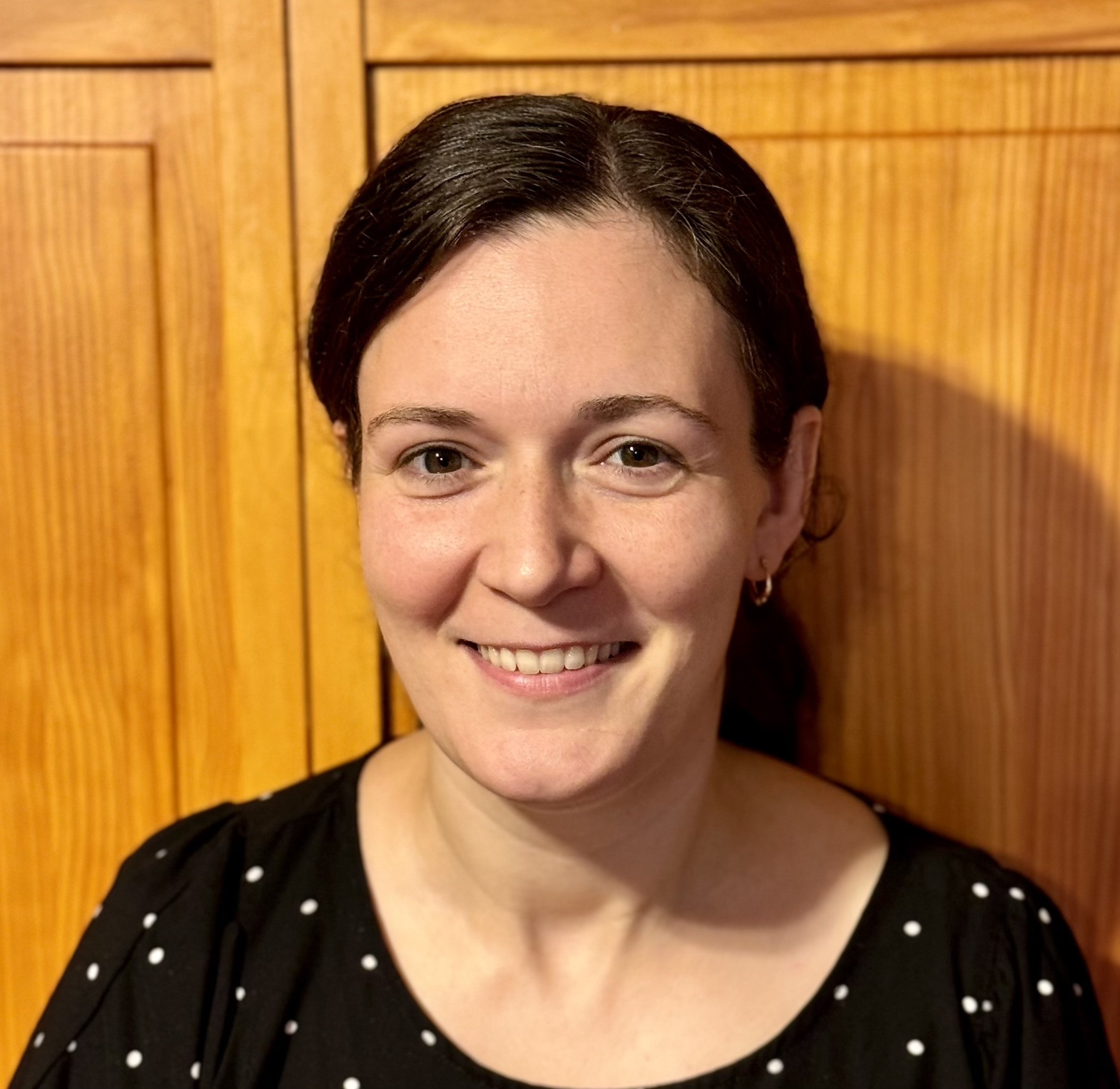 Headshot of Stephanie DeMora in front of a wooden background.