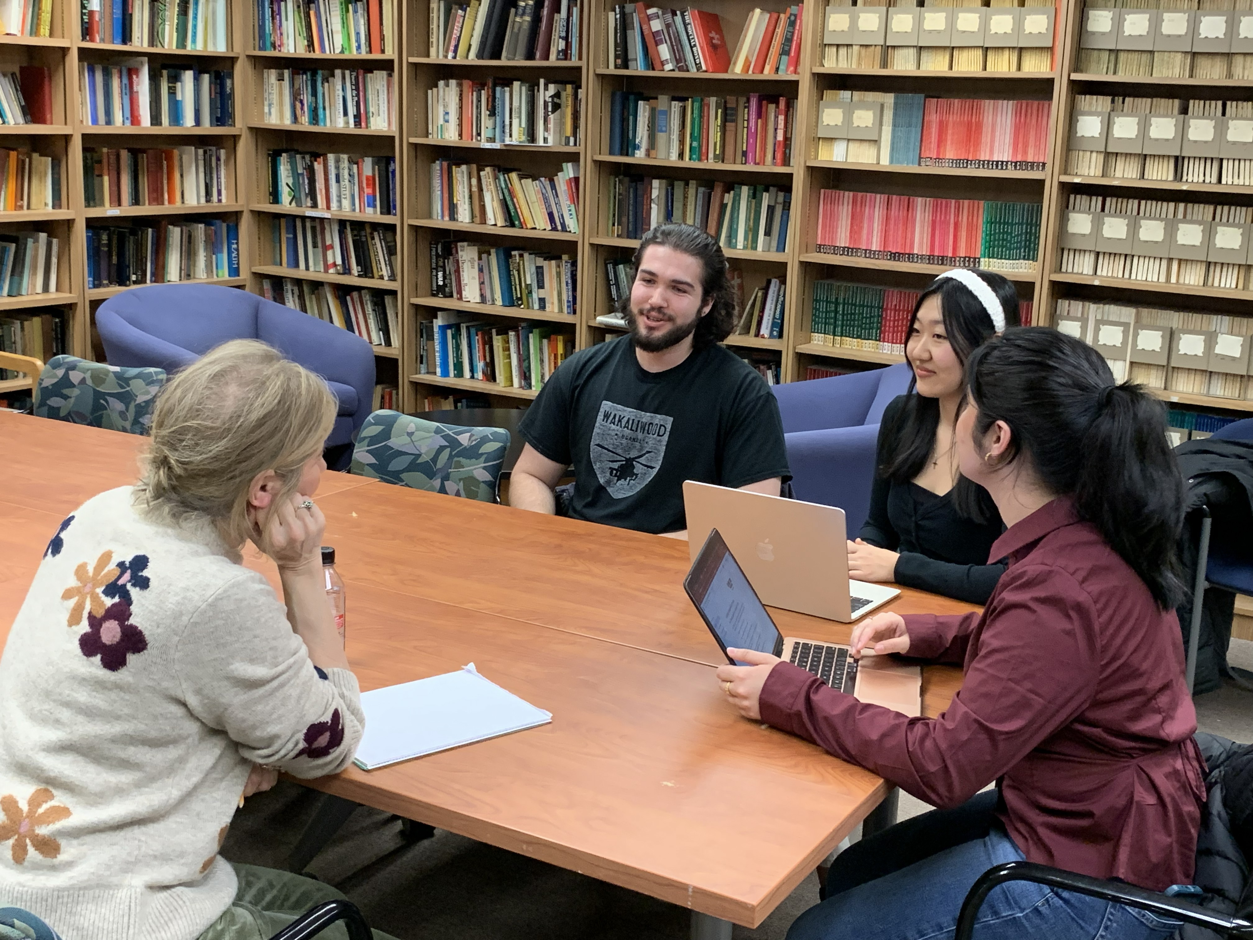 Faculty member sitting at a table with students talking in a library