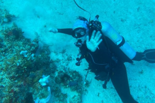 Ana Penavic waves at the camera while scuba diving
