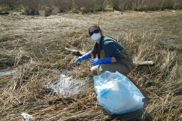 Cassie Bauer crouches in a marsh while wearing a mask Cassie Bauer crouches in a marsh while wearing a mask