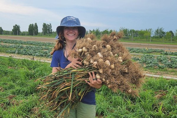 Viktoria Skobodzinski holds a buschel of garlic while smiling at the camera Viktoria Skobodzinski holds a buschel of garlic while smiling at the camera
